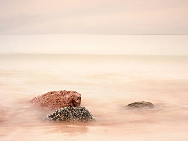 Long exposure of sea and big boulders sticking up from water within twilight time. — Stock Photo, Image