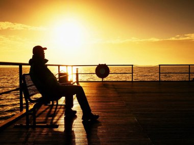 Turist wharf bankta oturup puslu güneşli sabah denize tadını çıkarın. Yumuşak su 