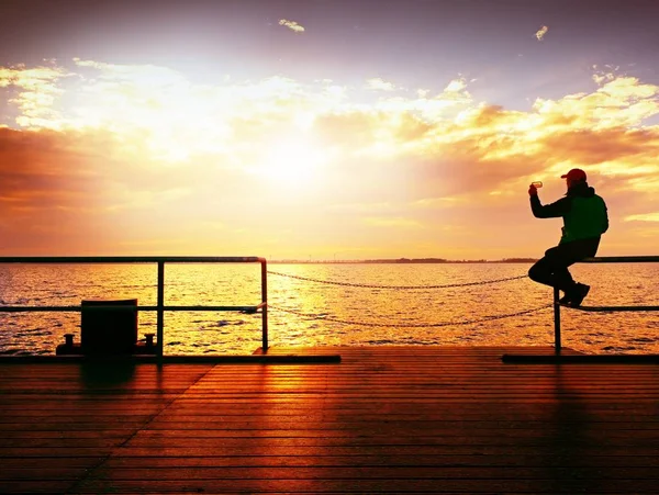 Tourist sit on mole handrail and takes pictures. Man enjoy morning at sea — Stock Photo, Image