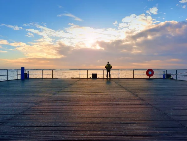 Un hombre solo en el muelle y mirar por encima de pasamanos en el agua. Cielo soleado, nivel de agua suave —  Fotos de Stock