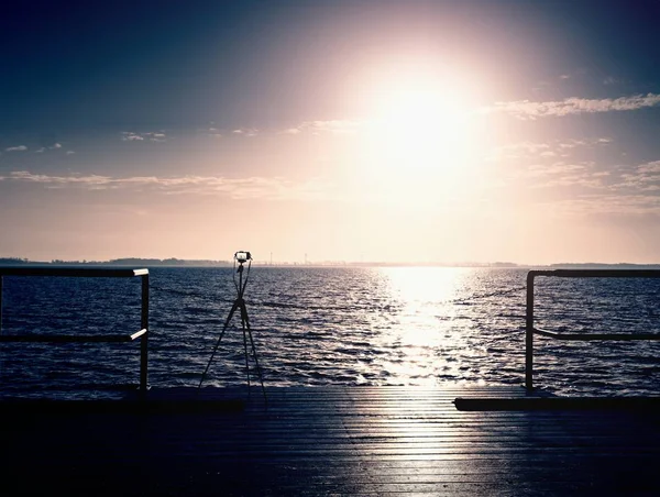 Stativ mit Kamera bereit auf Pier, Sonne über dem Ozean. Leere hölzerne Maulwurfplatte — Stockfoto