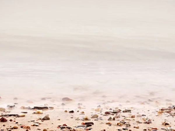 Çakıl kum plajındaki köpüklü deniz suyuna karşı. Doğal romantik offshore — Stok fotoğraf