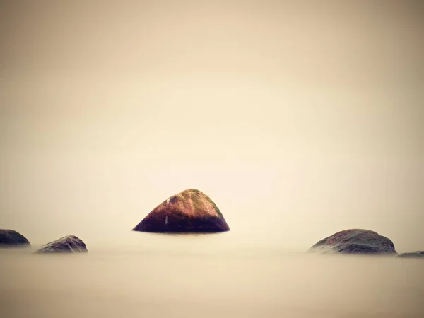 Grandi massi sporgenti dal mare ondulato liscio. Orizzonte rosa — Foto Stock