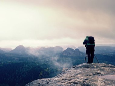 Sırt çantası ile yeşil ceketli fotoğrafçı fotoğraf cliff üzerinde alır.