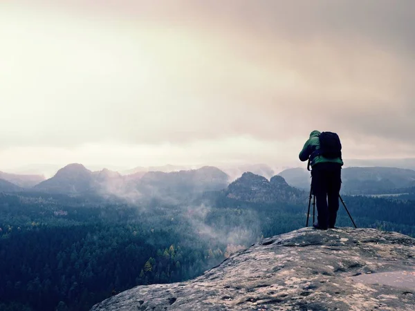 Photographer  in green jacket with backpack takes photos on cliff — Stock Photo, Image