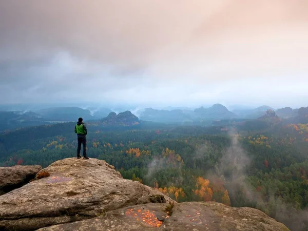 Caminante en verde windcheater, gorra y pantalón de trekking oscuro de pie en la montaña pico roca . — Foto de Stock