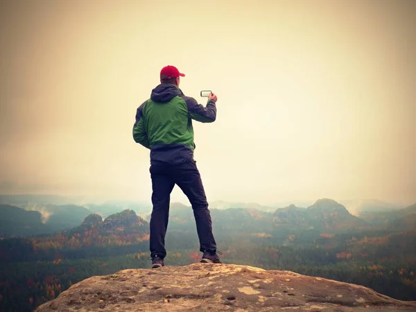 Homem tira fotos com telefone inteligente no pico do império rock. Névoa melancólica — Fotografia de Stock