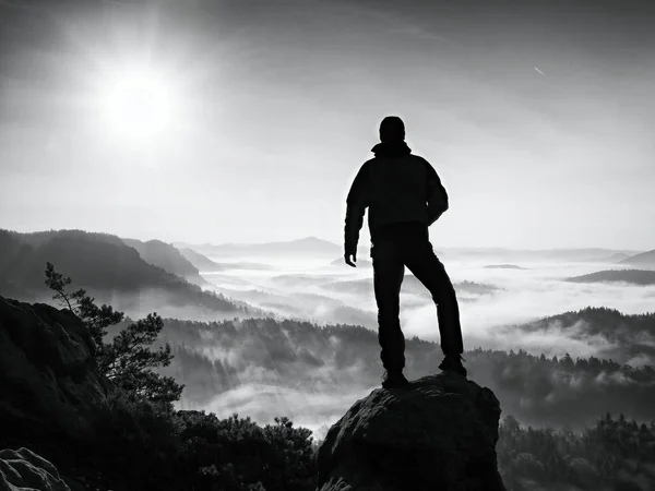 Turista se vyšplhal na vrchol skály nad údolím. Muž hodinky mlhavé a mlhavé ráno údolí — Stock fotografie