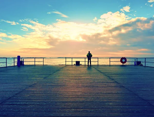 Yalnız adam iskele ve Küpeşte suya üzerinden bakmak. Güneşli gökyüzü, yumuşak su seviyesi