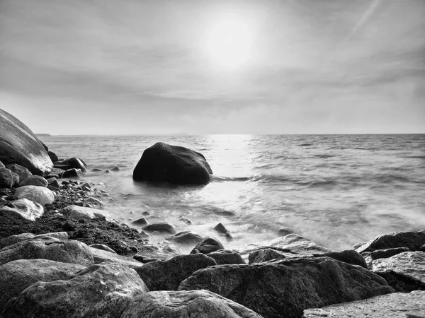 Boulders at island shore stick up from smooth sea. Stony coast defies to waves — Stock Photo, Image