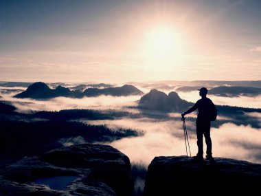 Hiker silhouette stand on cliff and watching over misty valley to Sun. Blue filtere clipart