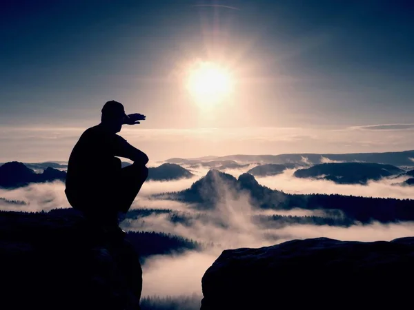 剪影的黑色和帽的独自徒步旅行者坐在悬崖上。蓝色滤光镜的照片。在追寻到 mis 的男人 — 图库照片