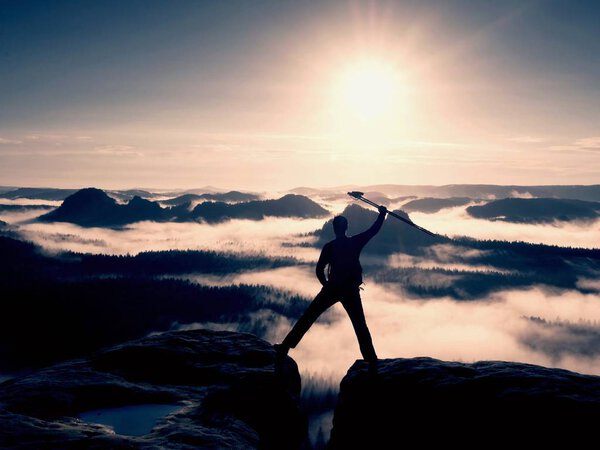 Hiker silhouette stand on cliff and watching over misty valley to Sun. Blue filtere