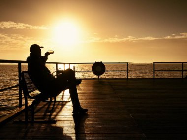 Turist wharf bankta oturup puslu güneşli sabah denize tadını çıkarın. Yumuşak su 