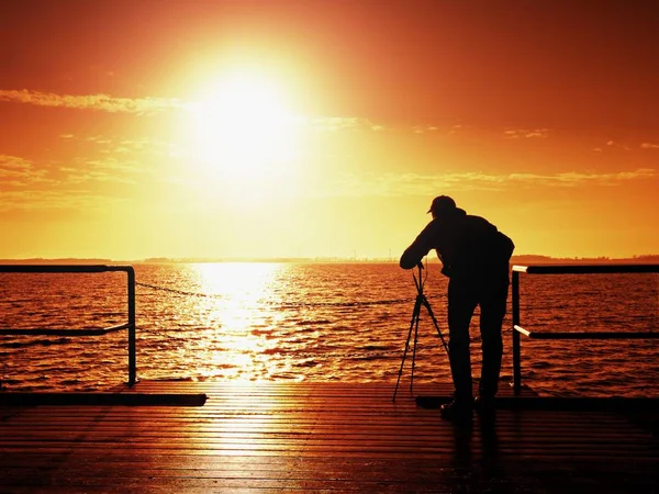 Man photograph with camera on tripod. Tourist at handrail on mole