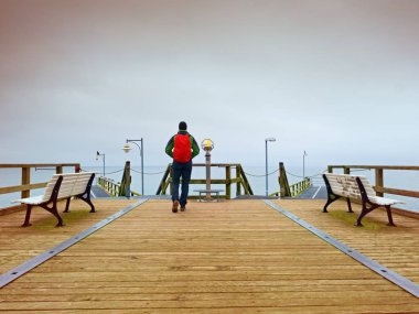 Turist ahşap deniz pier üzerine kırmızı sırt çantası ile. Trekking takım elbiseli adam