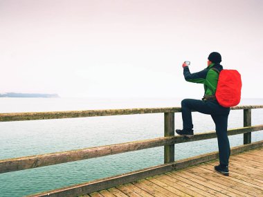 Turist ahşap deniz pier üzerine kırmızı sırt çantası ile. Trekking takım elbiseli adam