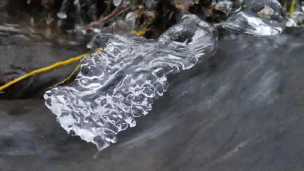 Detail es yang bersinar tergantung di atas air dingin sungai pegunungan musim dingin. Mengkilap es di atas sungai berbusa. Batang yang jatuh dengan penutup es dan serpihan kecil salju bubuk — Stok Video