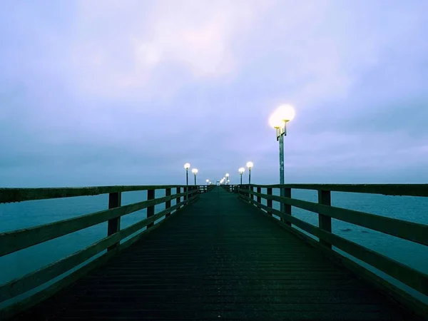 Pier op mistige nacht met gele lampjes op de achtergrond van een donker blauwe hemel — Stockfoto