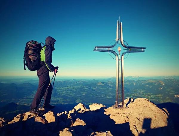 Hiker at big crucifix on mountain peak. Iron cross at Alps mountain top. — Stock Photo, Image