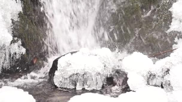 Iciciles bellow waterfall. Snowy and icy stones and boulders with drops of fallen chilly water. Fallen icicle bellow waterfall, stony and snowy stream bank. Close focus. — Stock Video