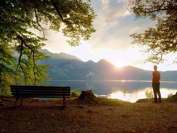 Man in red tshirt walk at lake bank.  Empty wooden bench, tree stump — Stock Photo, Image