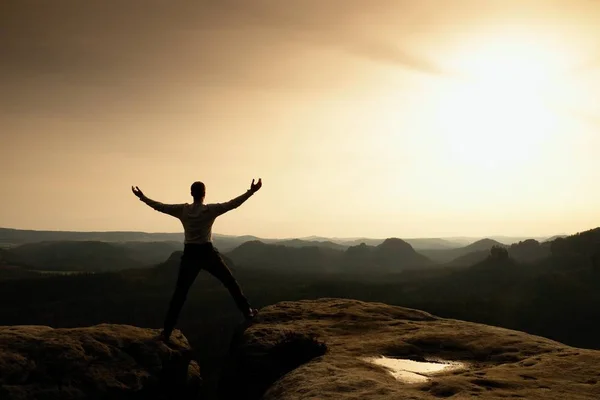 Glückliche Mann mit erhobenen Armen Geste Triumph auf exponierter Klippe. Wanderer befriedigen Silhouette auf Sandsteinfelsen mit Blick auf hügelige Landschaft. — Stockfoto