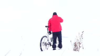 Under karlı dağ bisikleti olan adam. Motorcu Bisiklet derin karda bastırıyor. Nazik rüzgar ve küçük kar pul Hava bulutlu kış günü. 
