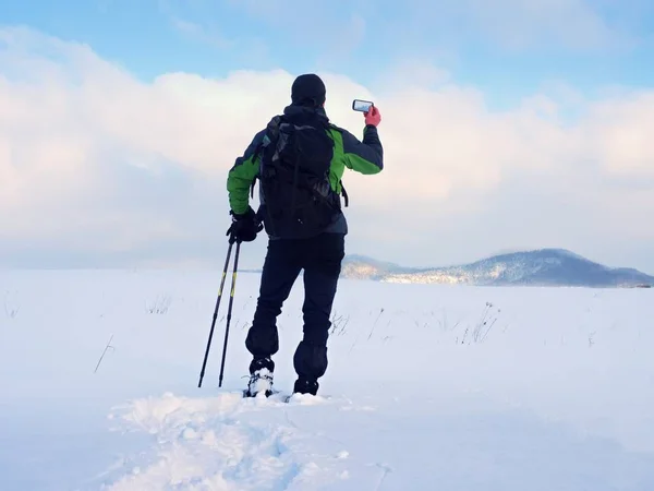 Άνθρωπος με χιονοπέδιλα και σακίδιο φωτογραφίες από smartphone. Πεζοπόρος σε χιονοστιβάδα — Φωτογραφία Αρχείου