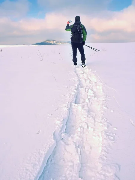 Man with snowshoes and backpack take photos by smartphone. Hiker in snowdrift — Stock Photo, Image