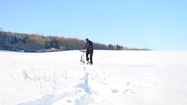 Motociclista empujando bicicleta de montaña en la nieve drift.Freeze clima soleado invierno. Motociclista está empujando bicicleta en la nieve profunda en el prado. Pequeños copos de nieve en el aire . — Vídeo de stock