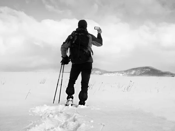 Hombre con raquetas de nieve y mochila tomar fotos por teléfono inteligente. Caminante en la deriva de nieve —  Fotos de Stock