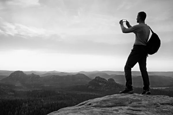 Tall backpacker with phone in hand. Spring daybreak in mountains. — Stock Photo, Image