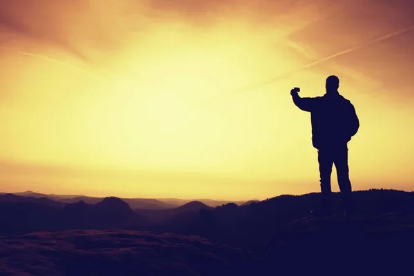 Mann in den Bergen für einen Abendspaziergang mit Trekkingstöcken. Sportler in Schwarz mit Händen in Taschen stehen auf dem Gipfel im Park der Felsenimperien und wachen über das neblige Morgental zur Sonne. Silhouette des Menschen. — Stockfoto