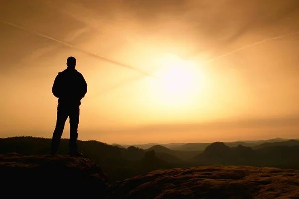 Sportsman no preto com as mãos nos bolsos estão no pico no parque dos impérios da rocha e observando sobre o vale nebuloso e nebuloso da manhã ao sol. Silhueta do homem . — Fotografia de Stock