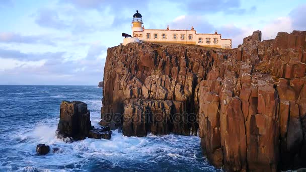 Belo farol Neist Point na costa oeste da Ilha de Skye, na Escócia, durante um pôr-do-sol tempestuoso. Farol brilhando ficar acima do mar das Hébridas, ondas batendo contra a rocha e penhasco . — Vídeo de Stock