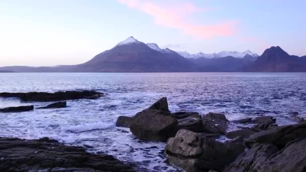 Tarde en la bahía de Elgol en la costa oeste de la isla de Skye en Escocia durante una puesta de sol ventosa. Montañas nevadas en la isla Soay sobre el mar de las Hébridas, olas estrellándose contra rocas y rocas afiladas — Vídeos de Stock