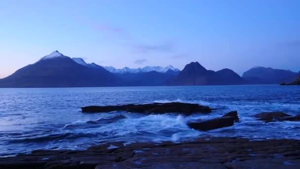 Noite na baía de Elgol, na costa oeste da Ilha de Skye, na Escócia, durante um pôr-do-sol ventoso. Montanhas nevadas na ilha de Soay acima do mar das Hébridas, ondas batendo contra pedras e rocha afiada — Vídeo de Stock