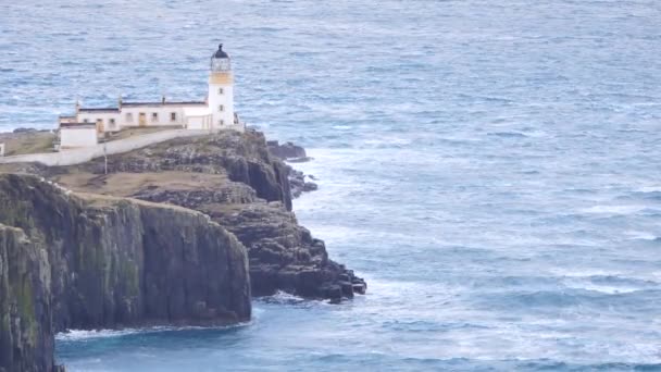 Belo farol Neist Point na costa oeste da Ilha de Skye, na Escócia, durante um pôr-do-sol tempestuoso. Farol brilhando ficar acima do mar das Hébridas, ondas batendo contra a rocha e penhasco . — Vídeo de Stock