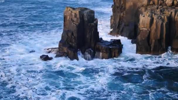 Grandes ondas fortes batendo contra a rocha afiada da Ilha de Skye, na Escócia. Nível do mar espumoso. Pedras pretas grandes arredondadas e torre rochosa aguda acima do mar espumoso das Hébridas. Resort turístico . — Vídeo de Stock