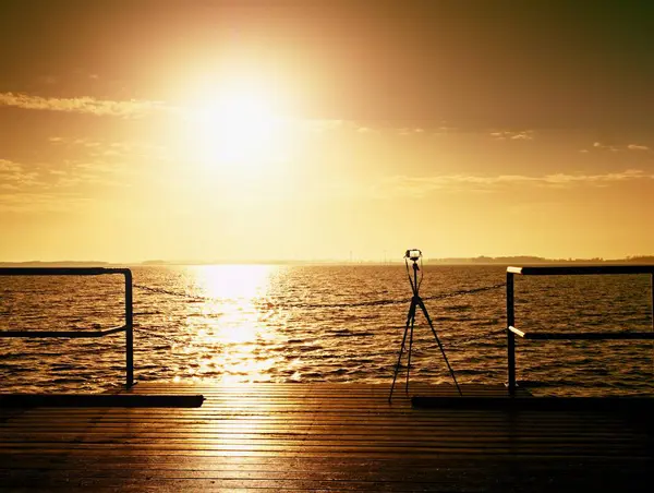 Tripé com câmera pronta no cais, Sol acima do oceano. Placa de toupeira de madeira vazia — Fotografia de Stock