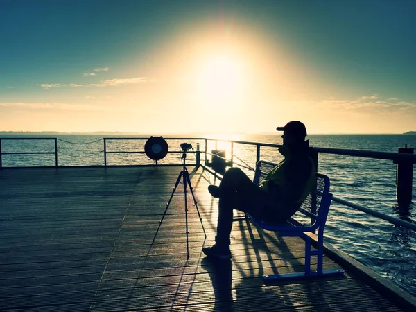 Hobby photograph sit on bench at camera on tripod. Wooden board quay — Stock Photo, Image