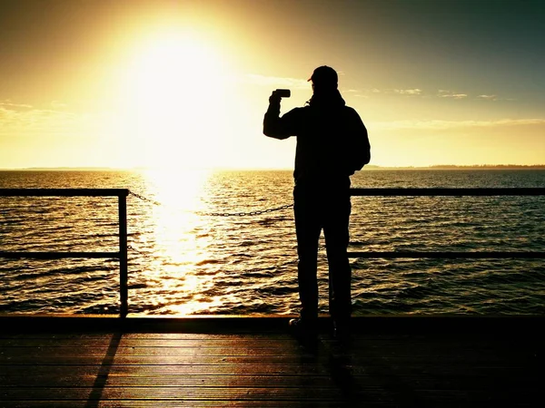 Smartphone-Künstler fotografiert über Handlauf auf Maulwurfsonne über dem Meer — Stockfoto