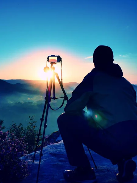 Amatör fotograf tar bilder med spegel kamera på toppen av rock. Drömmande fogy landskap, våren orange rosa dimmiga soluppgång i en vacker dal nedan — Stockfoto