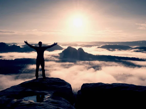 Силуэт туриста стоит на скале и наблюдает за туманной долиной до Солнца. Синий фильтр — стоковое фото