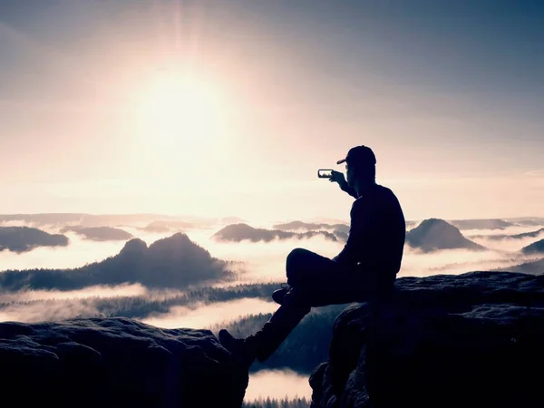 Silhouette di escursionista solo in nero e cappello sedersi sulla scogliera. Foto filtro blu. L'uomo che guarda male — Foto Stock