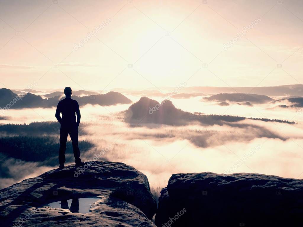 Hiker silhouette stand on cliff and watching over misty valley to Sun. Blue filtere