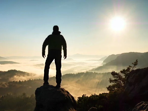 Mann, der hoch oben auf Klippe steht. Wanderer erklimmt felsigen Gipfel und genießt Aussicht — Stockfoto