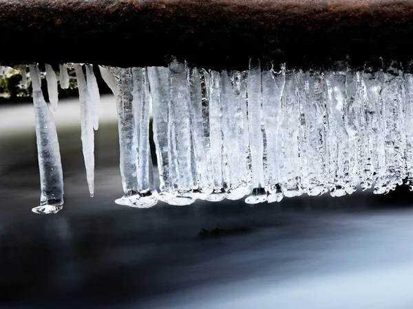 Long icicles hang above dark freeze  water of mountain stream. — Stock Photo, Image