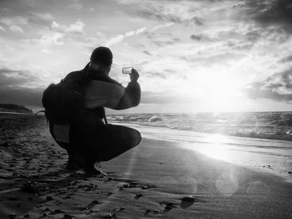 Mann fotografiert Abendmeer. Wanderer mit Rucksack und Handy in der Hand. Touristenbesetzung — Stockfoto